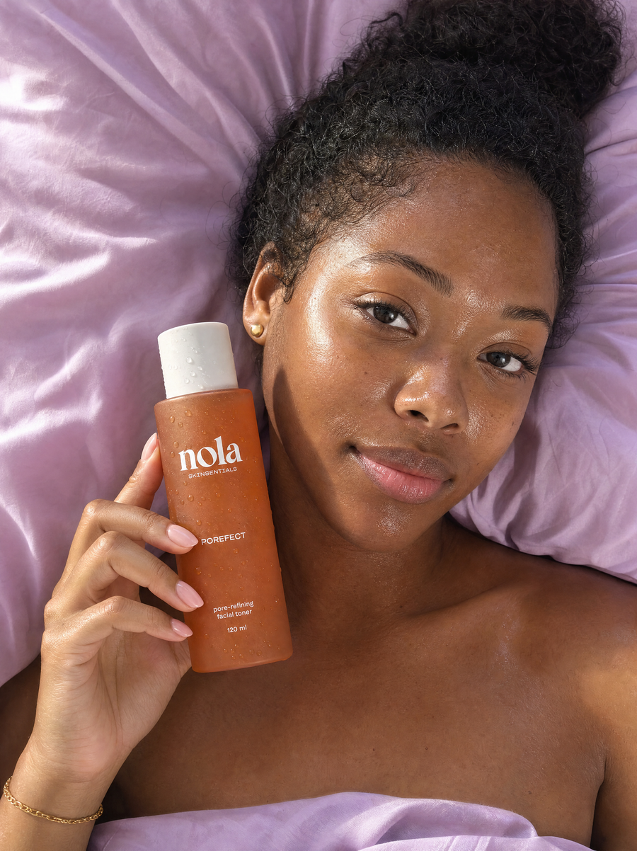 Woman in bed holding Porefect toner with dewy skin and droplets on the bottle.