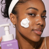 Woman holding the Clarifying Cleansing Foam bottle with foam in her hand.