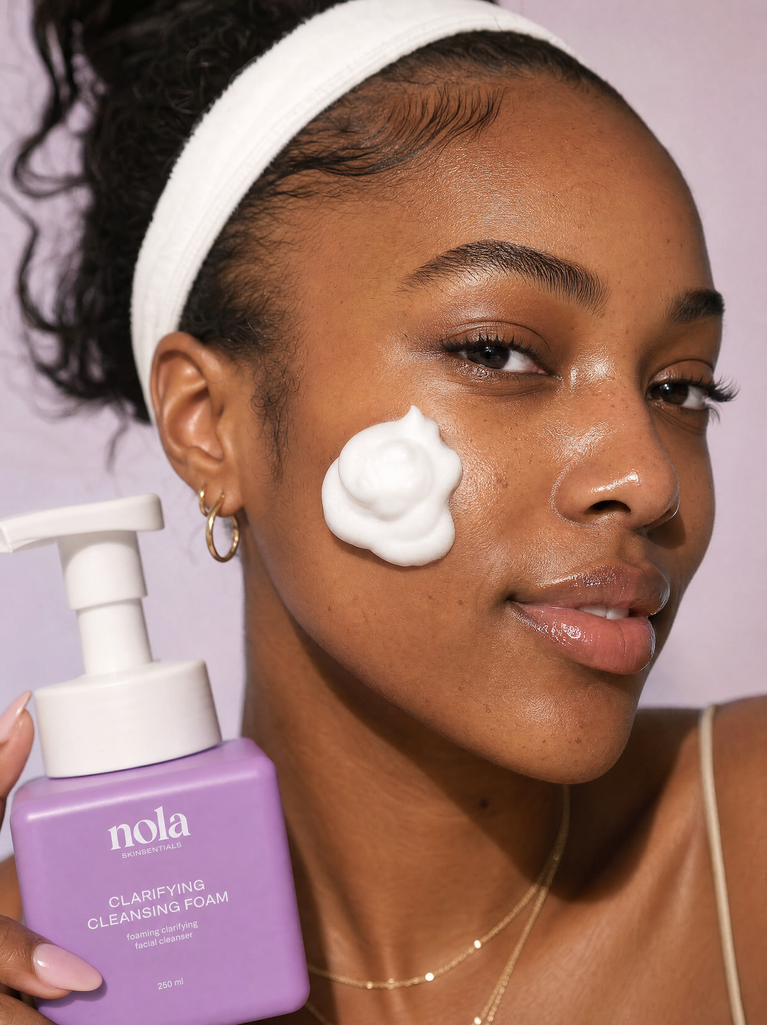 Woman holding the Clarifying Cleansing Foam bottle with foam in her hand.