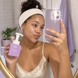 Woman holding Clarifying Cleansing Foam in her bathroom mirror selfie.