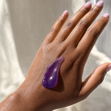 Purple jelly cleanser texture on the back of a hand in natural light.