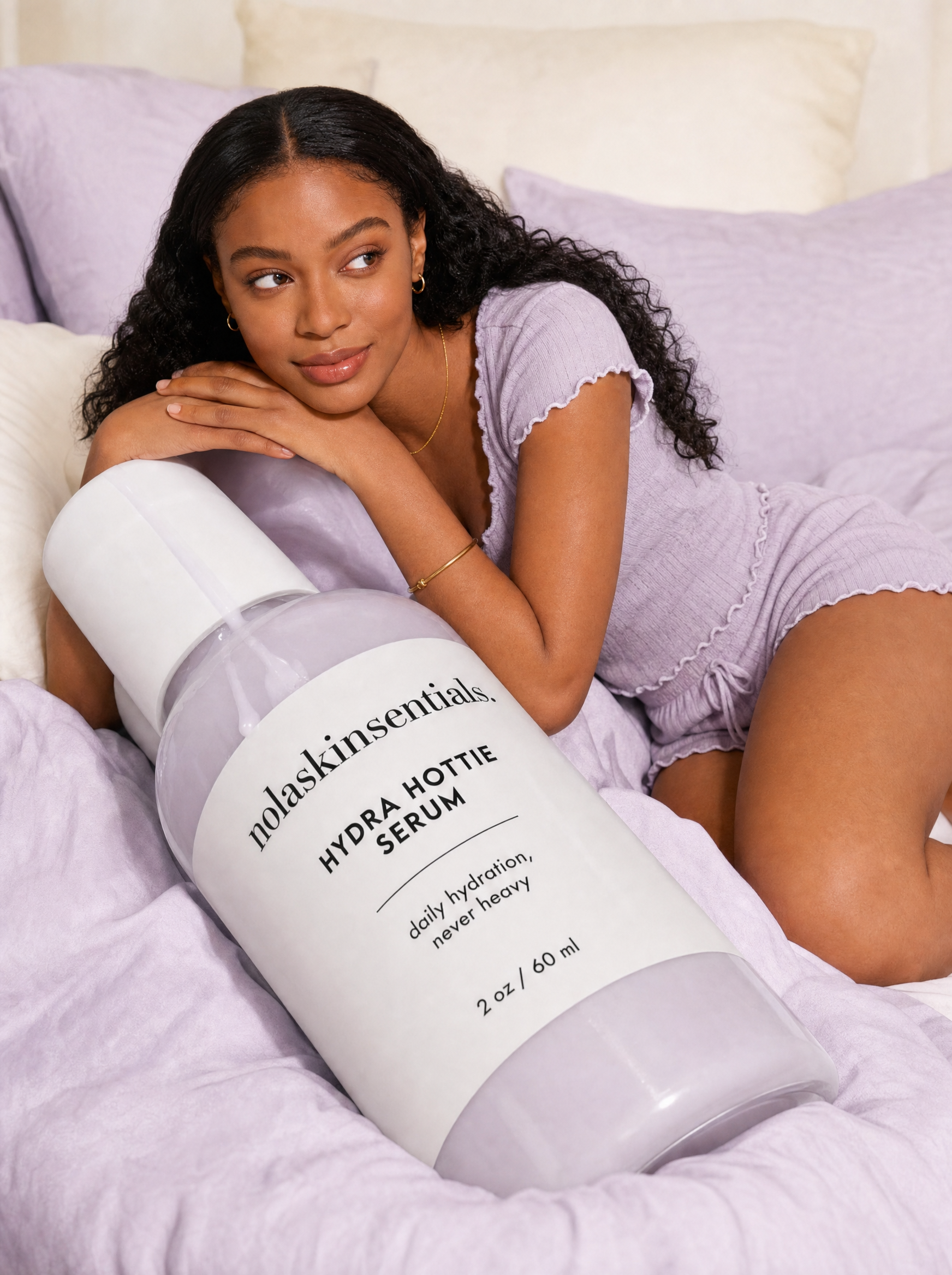 Model in lavender pajamas relaxing with Hydra Hottie Serum bottle by NOLA Skinsentials